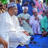 Hon. Umar Yusuf Yabo seated in a patterned cap and white robe, gesturing with one hand, with men seated behind him.
