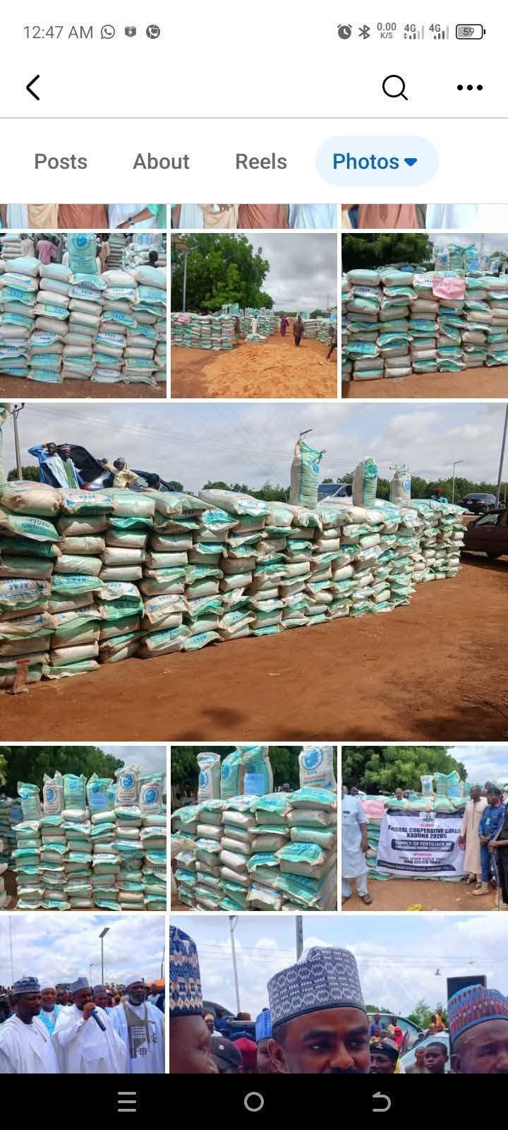 Screen capture from a photo album: pallets of bagged fertiliser stacked on sandy ground, with men standing among them and vehicles parked behind.