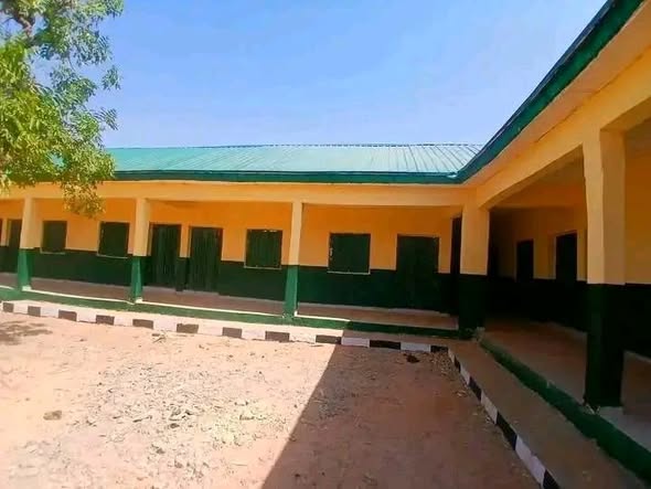 The courtyard of a renovated classroom block: cream walls over a dark green dado, a green corrugated roof, green doors and barred windows along the covered verandah.
