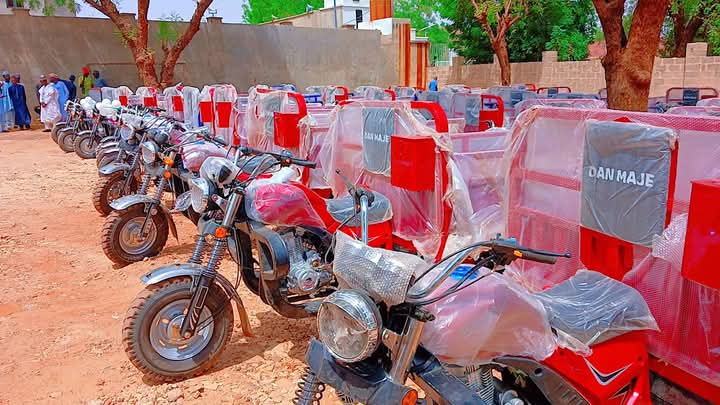 A second angle on the same distribution: motorcycles with balloons on the handlebars, the “DAN MAJE” tricycle boxes behind them, and attendees gathered along the line.
